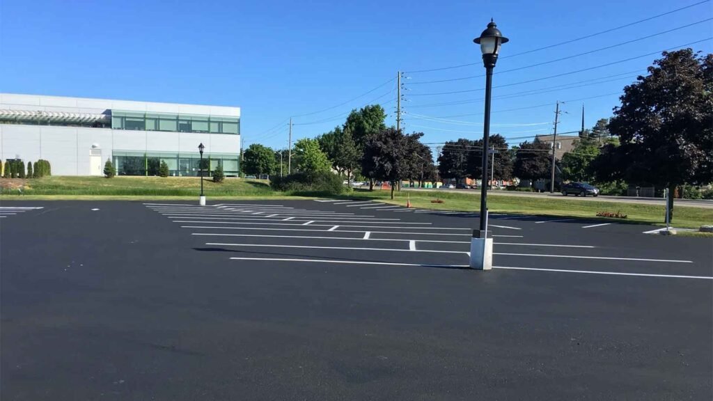 Empty parking lot with white parking space lines in front of a modern commercial building on a sunny day.