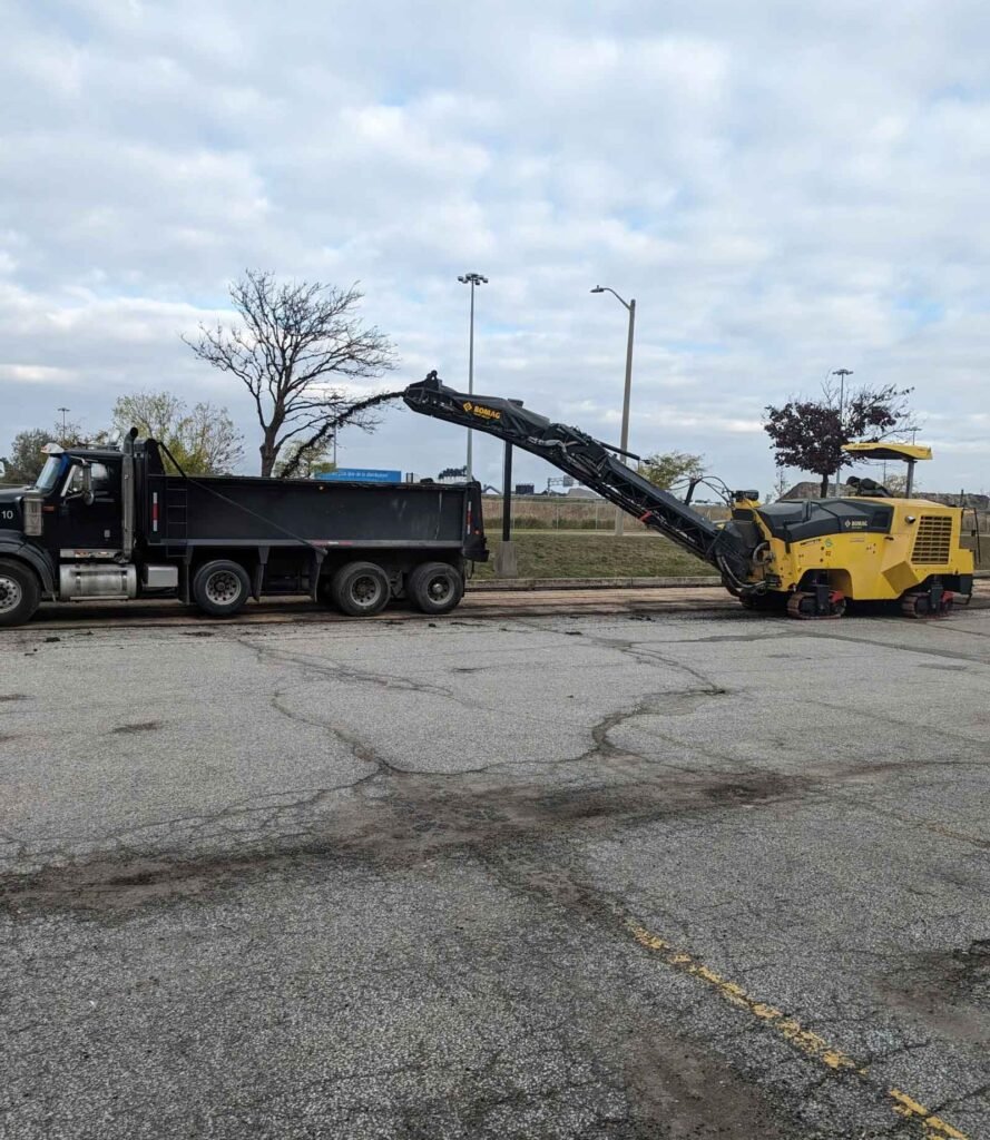 Excavator unloading into a dump truck next to a yellow pavement roller on a cloudy day.