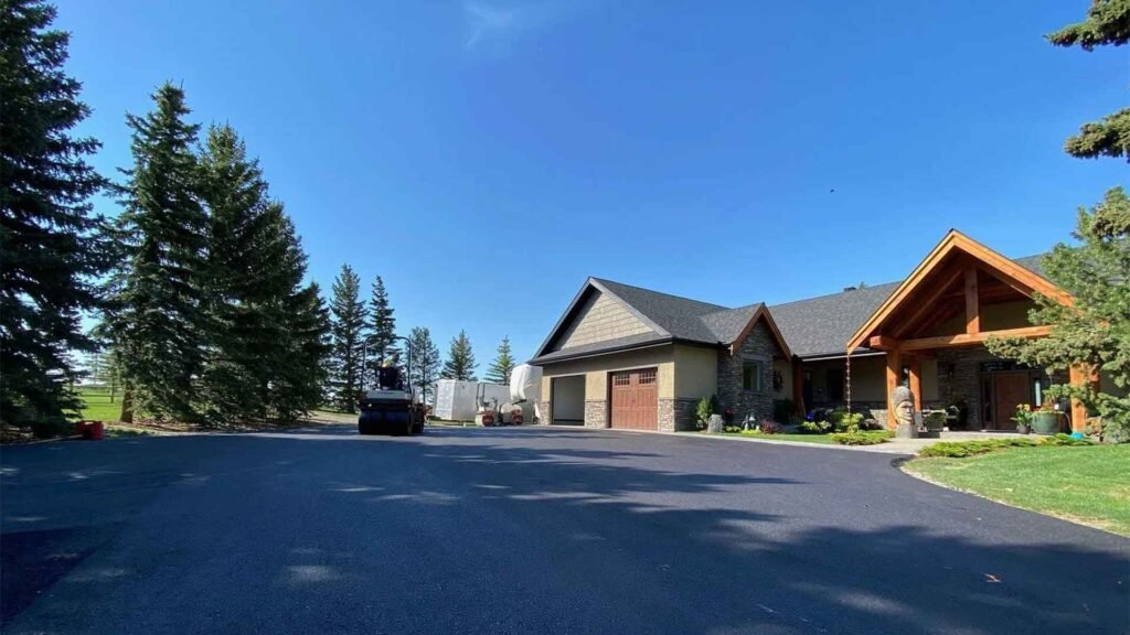 Freshly paved driveway at a rustic house with clear blue skies and lush pine trees.