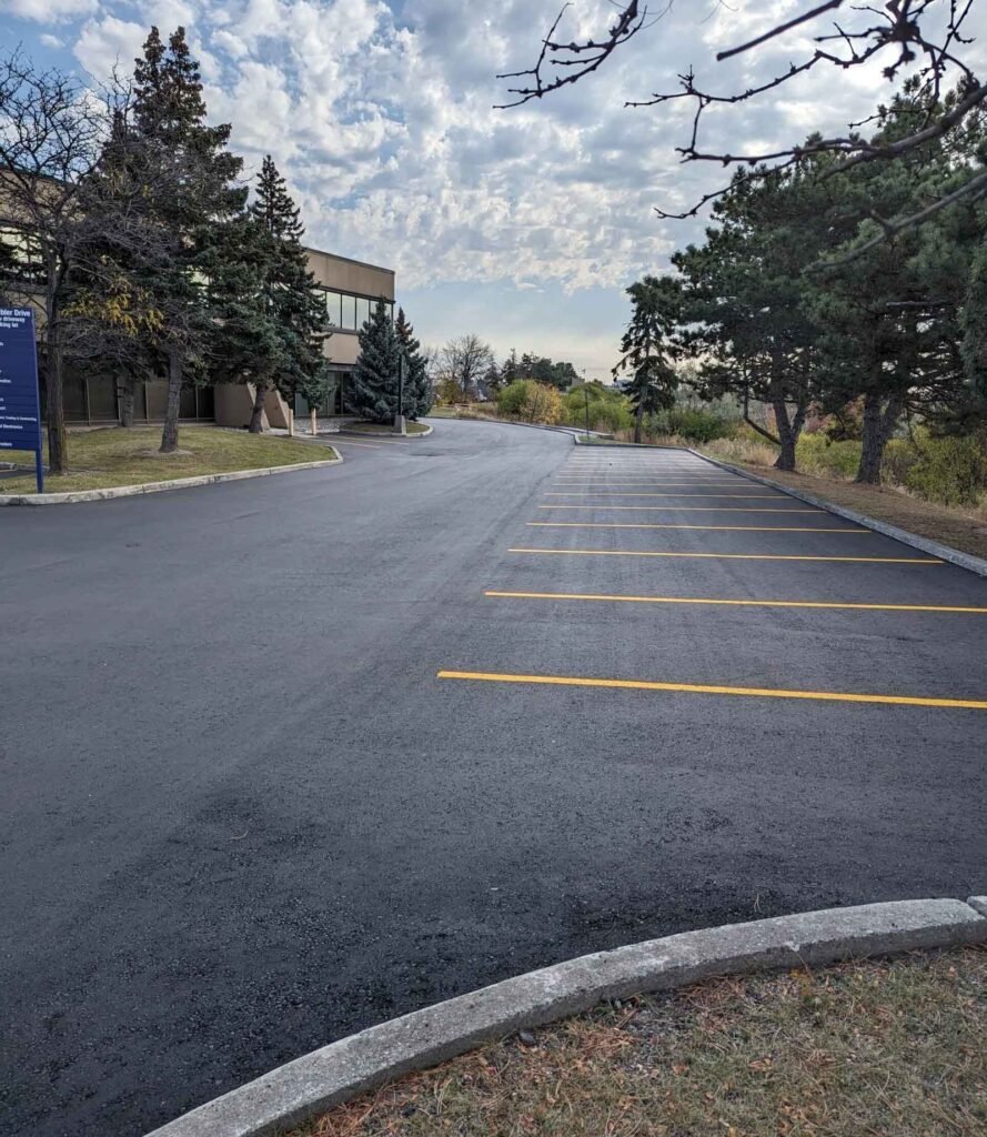 New asphalt parking with bright yellow lines in front of an office building under a cloudy sky.