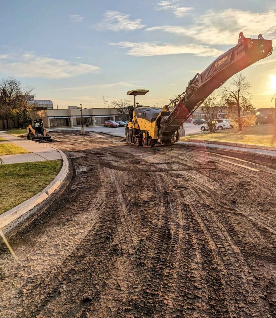 Sunset at construction site with paving equipment and excavator near office buildings.