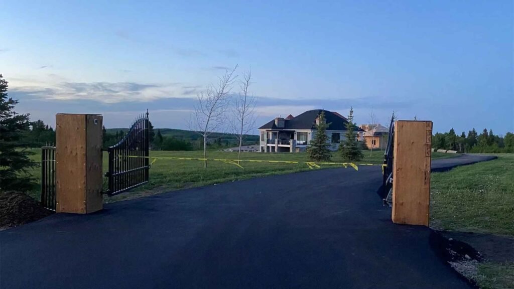 Twilight view of a new driveway leading to a large house with open gates and a rural landscape.